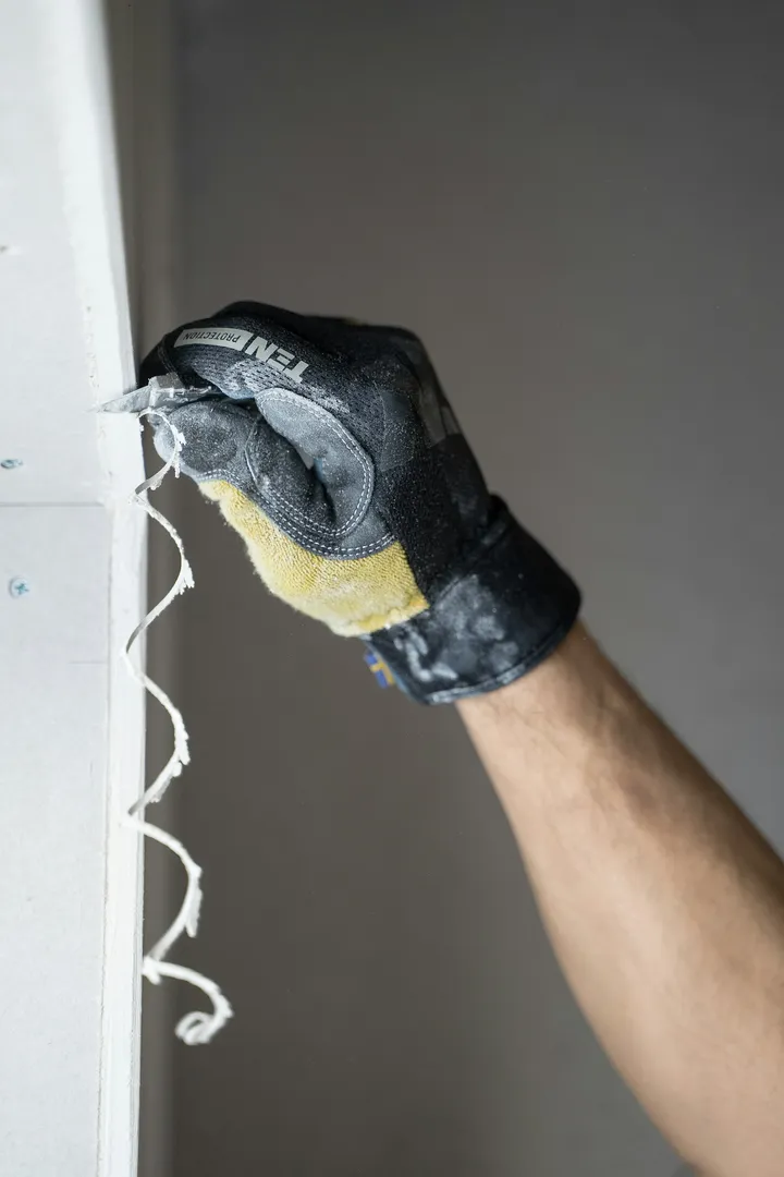 A gloved hand finishing a drywall edge with joint compound during a wall repair