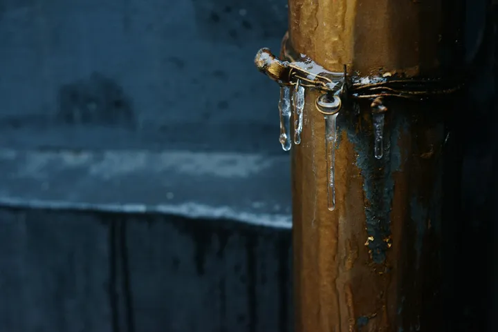 Iced-over exterior metal water pipe with icicles forming during a hard winter freeze
